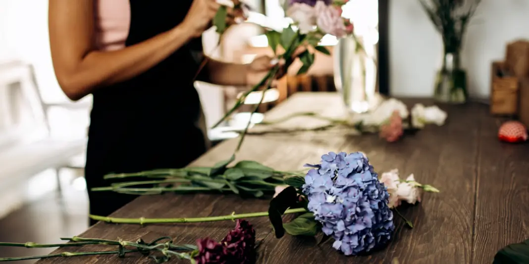 A florist is preparing flowers on a wooden table.